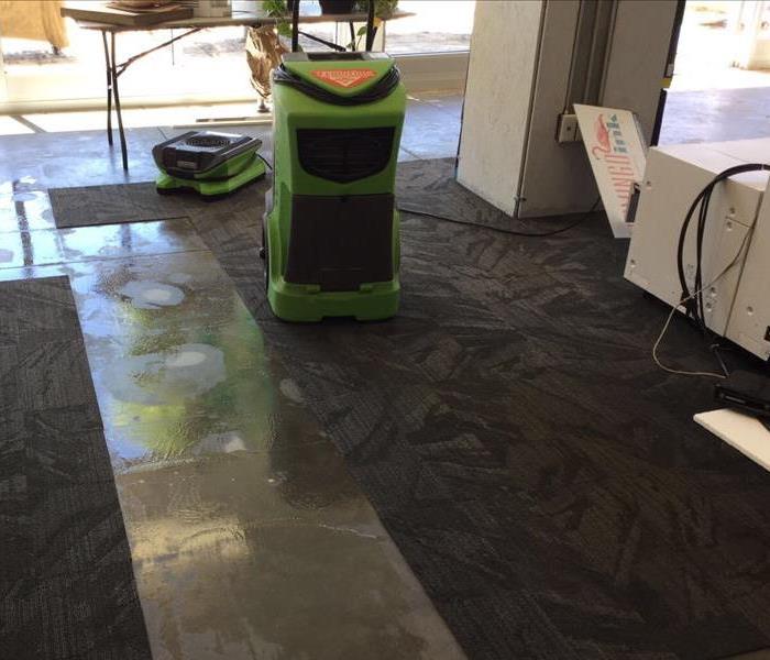 office with water damage on flooring with green air mover and dehumidifier working to dry the area